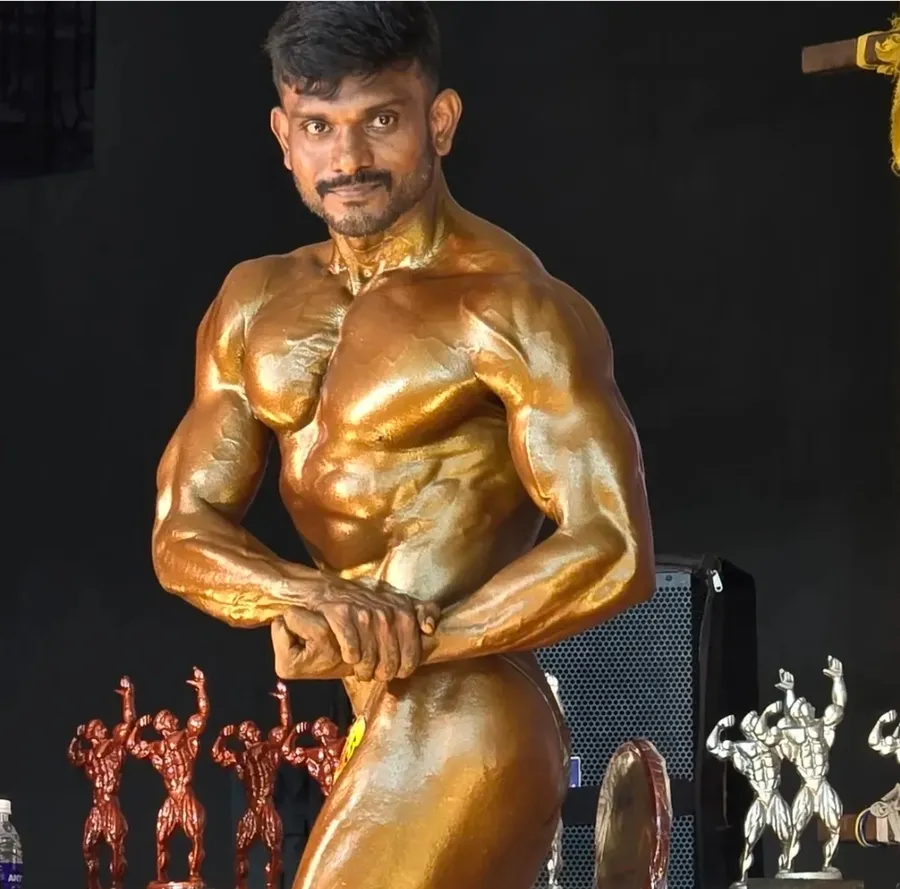 Jaya Prakash, founder of JP Fitness, posing on stage at a bodybuilding competition with trophies